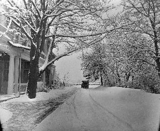 A photograph of a house, a driveway and a car during winter.