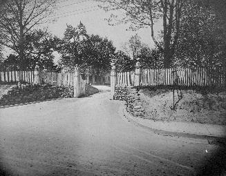 A photograph of a road and a fence in the background with an open gate.
