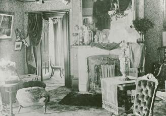 A photograph of the interior of a house, with a fireplace, chairs and other pieces of furniture ...