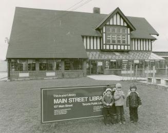 Three smiling children in front of the sign for Main Street library approximately 1977.