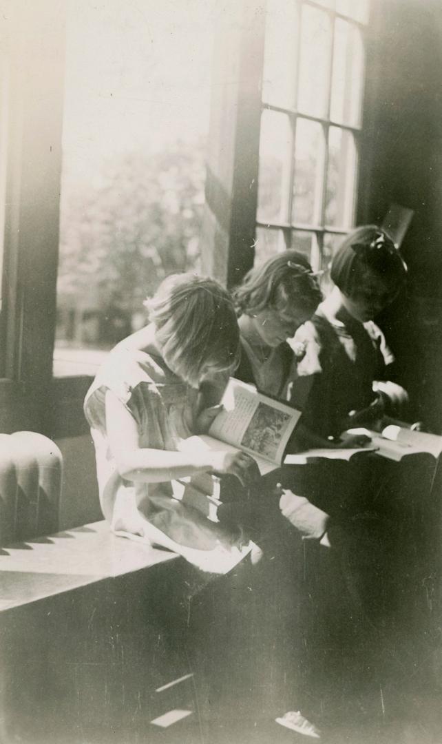 Three children sitting on a bench in a shaft of sunlight reading books