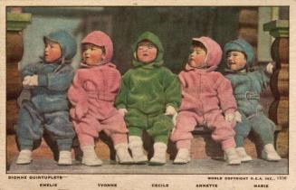 Color photograph of five toddlers in snowsuits sitting on the step of a log structure.