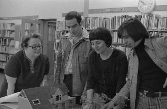 Four people gathered around a table looking a the architects model for Main Street library.