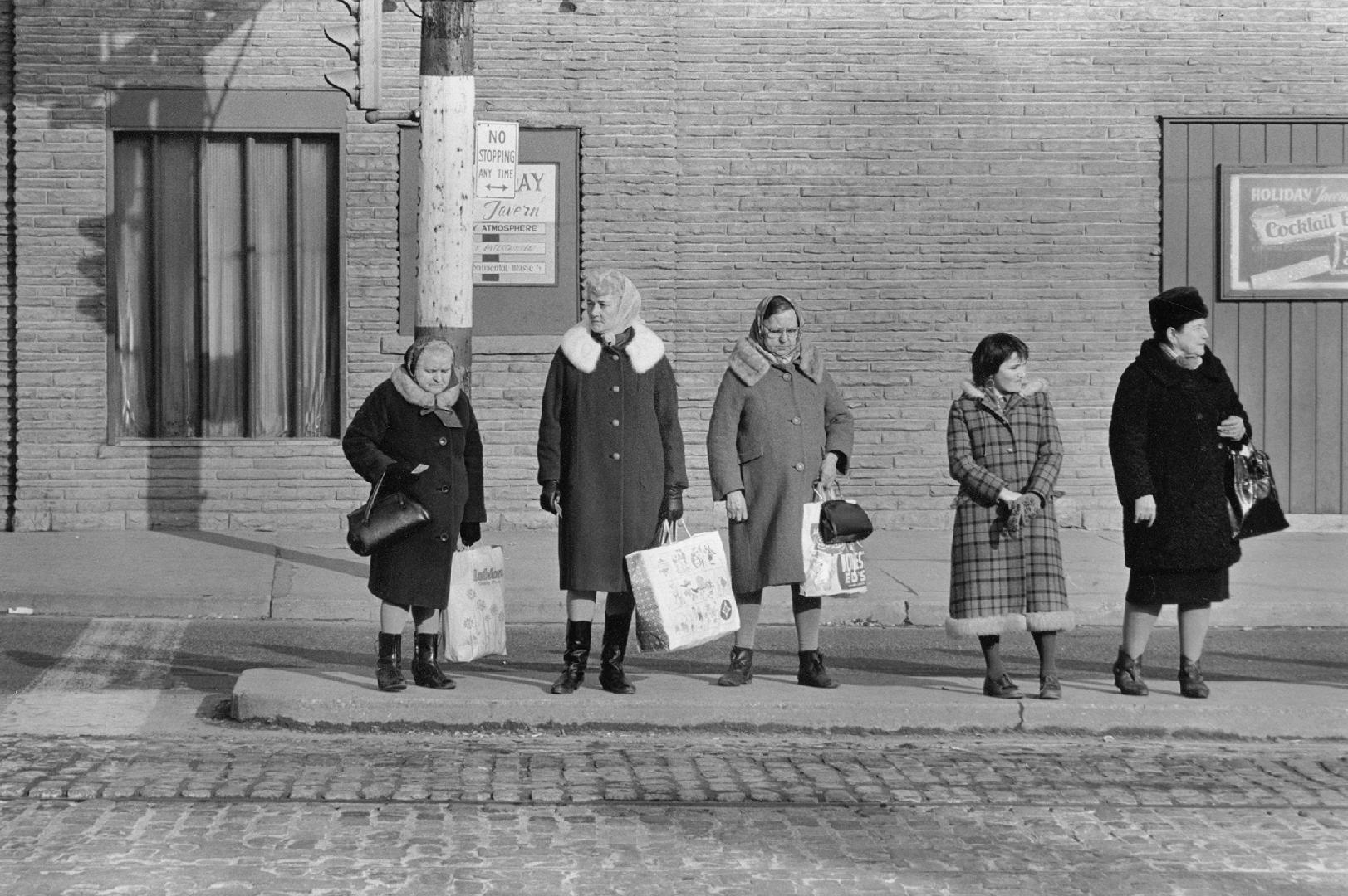 A photograph of five women standing on a sidewalk near a traffic light.