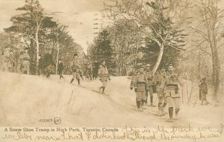 Sepia toned photograph of a group on men on snowshoes walking in a snowy, wooded area.