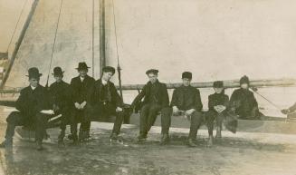 Black and white photograph of eight men sitting on a stationary ice boat.