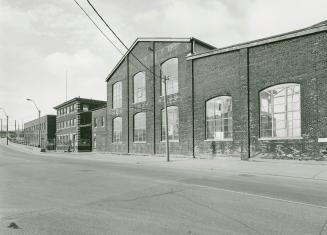 A photograph of a factory street facade, with a sidewalk, street and lamppost visible.