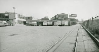 A photograph of a loading dock, with transport trucks parked outside and railroad tracks visibl ...