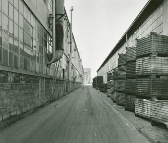 A photograph of a laneway between two factory buildings.