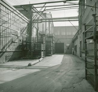 A photograph of a factory courtyard, with a doorway visible and shelving units piled next to it ...