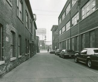 A photograph of a laneway between two buildings, with cars parked outside and a Nissan billboar ...