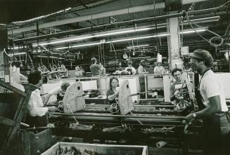 A photograph of factory workers building washing machines on an assembly line.