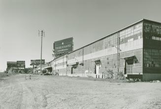 A photograph of a factory building, with cars parked beside it and a billboard for Apple Comput ...
