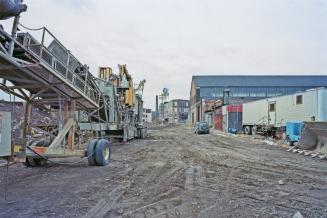 A photograph of a dirt laneway between buildings and construction trailers on the right side an ...