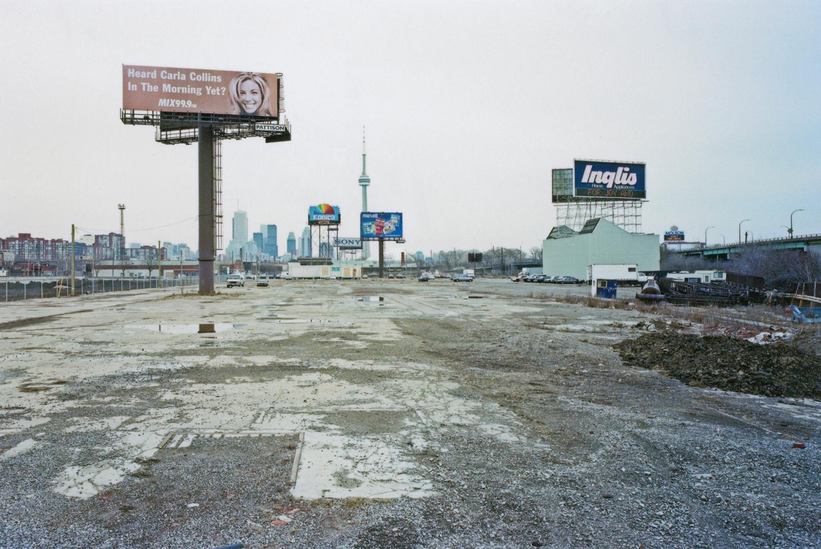 A photograph of a muddy parking lot. A building to the left has an Inglis billboard above it. T ...