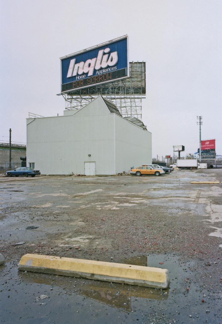 A photograph of a building surrounded by a parking lot, with an Inglis billboard above it.