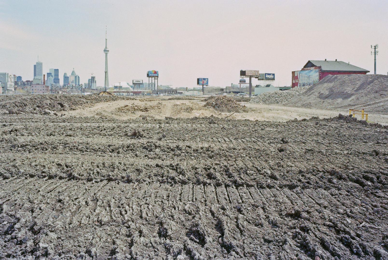 A photograph of a muddy field, with a shed visible to the right and the Toronto skyline includi ...