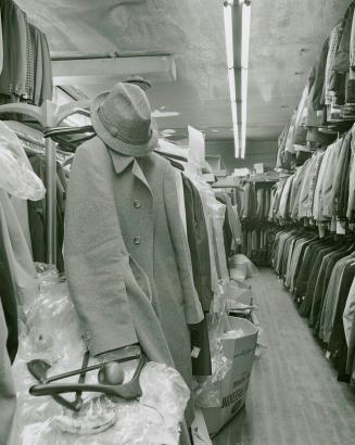 A photograph of a clothing store, with a coat, hat and apple in the foreground and racks of clo ...