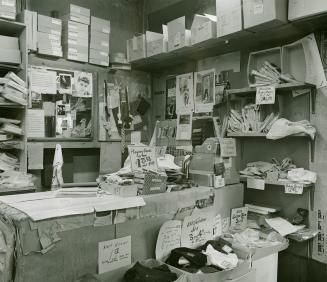 A photograph of a cash register on a sales counter, with boxes of playing cards and clothing vi ...