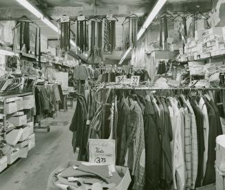 A photograph of a clothing shop, with racks of vests, coats, ties and other articles of clothin ...