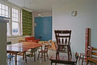 A photograph of a classroom, with chairs and desks in a room with windows and a clock on the wa ...