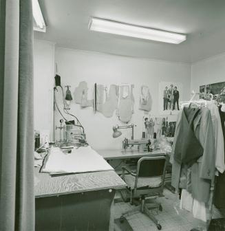 A photograph of a small room containing a sewing station, a chair and a rack of clothing.