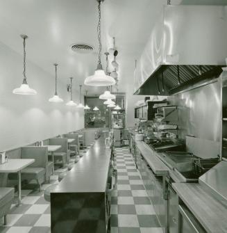 A photograph of a diner, with a kitchen area, counter, stools and tables visible.