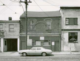 A photograph of an empty storefront, with a car parked in front of it.