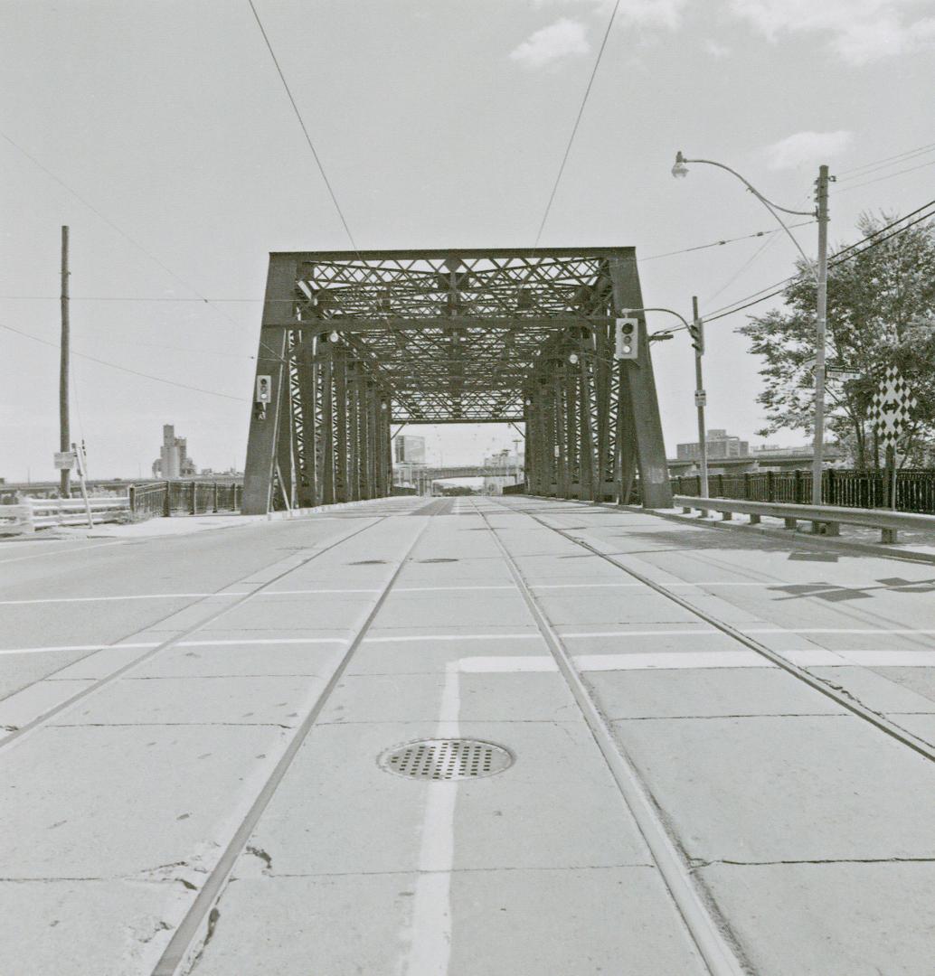 A photograph of a bridge with a road running through it, with streetcar tracks in the middle of…