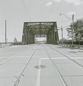 A photograph of a bridge with a road running through it, with streetcar tracks in the middle of…