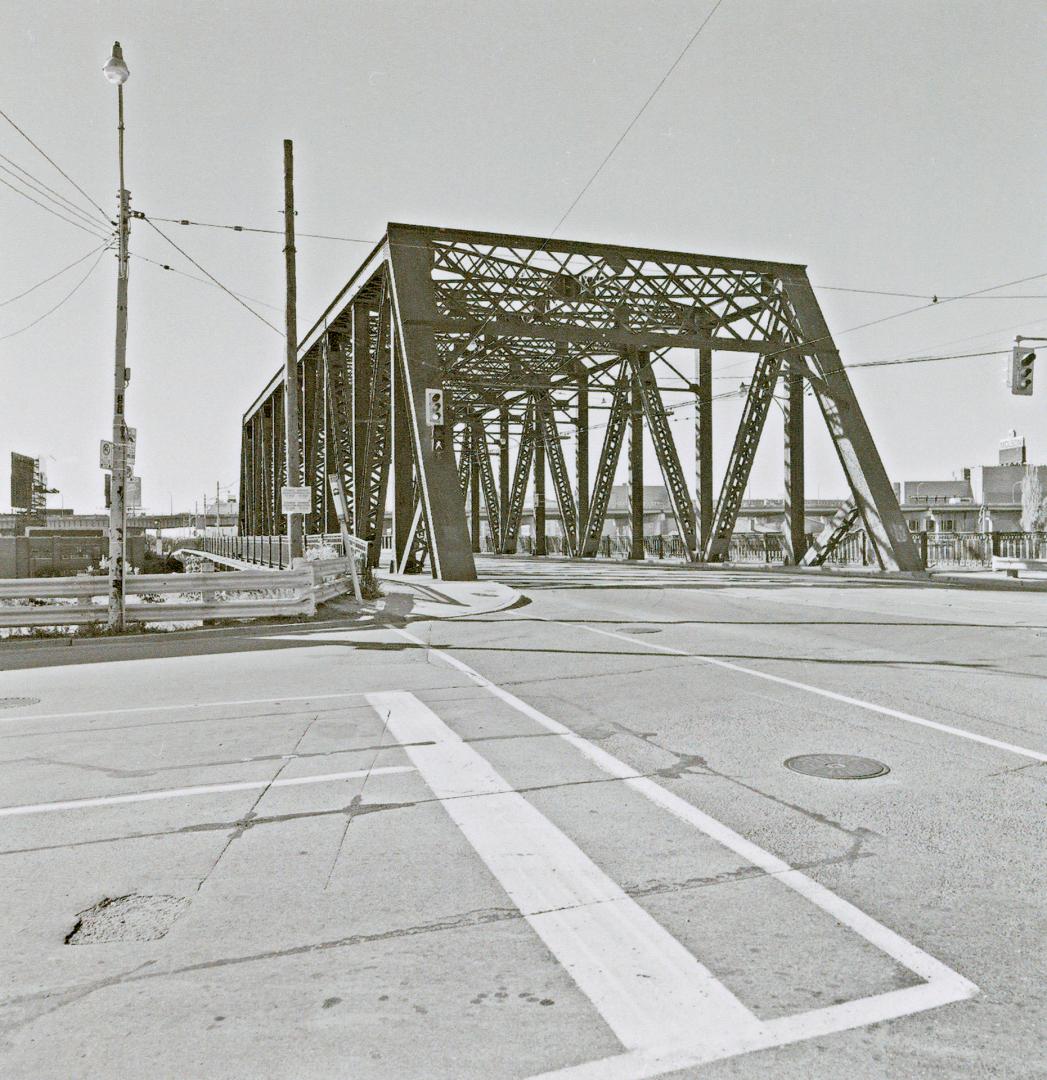 A photograph of a bridge with a road running through it and streetcar tracks in the middle of t…