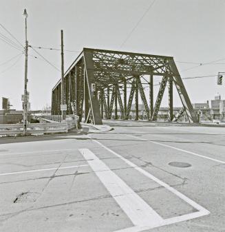 A photograph of a bridge with a road running through it and streetcar tracks in the middle of t…