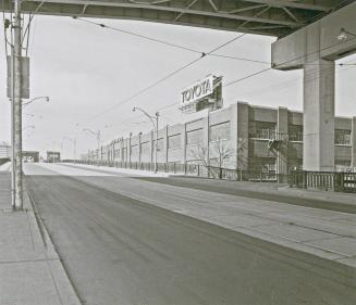 A photograph of a road under an elevated highway. A building with a &quot;Toyota&quot; sign is  ...