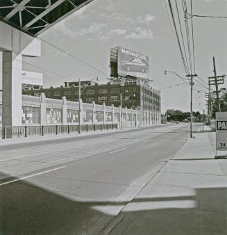 A photograph of a road under an elevated highway. There is a building with a billboard advertis ...