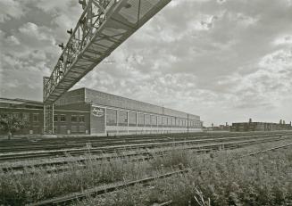 A photograph of a factory building, with railway tracks and light signals in the foreground.