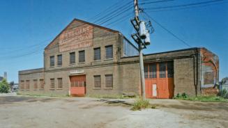 A photograph of a derelict building, with a telephone pole and wires in front of it and a sign …