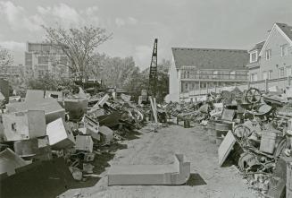 A photograph of a yard, with piles of old machinery, other metal objects, a crane, and resident ...