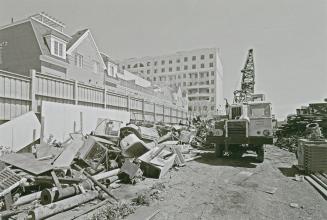 A photograph of a yard with piles of various metal objects and a crane, with residential houses ...