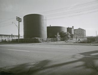 A photograph of storage tanks, with a road in the foreground and buildings in the background.