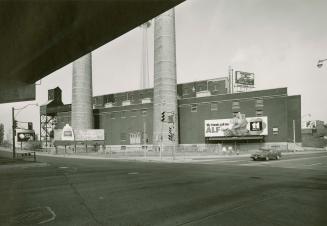 A photograph of an industrial facility with two smokestacks and a parking lot in the foreground ...