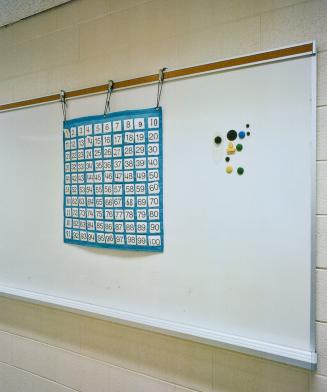 A photograph of a whiteboard, with magnets and a grid containing the numbers from one to one hu ...