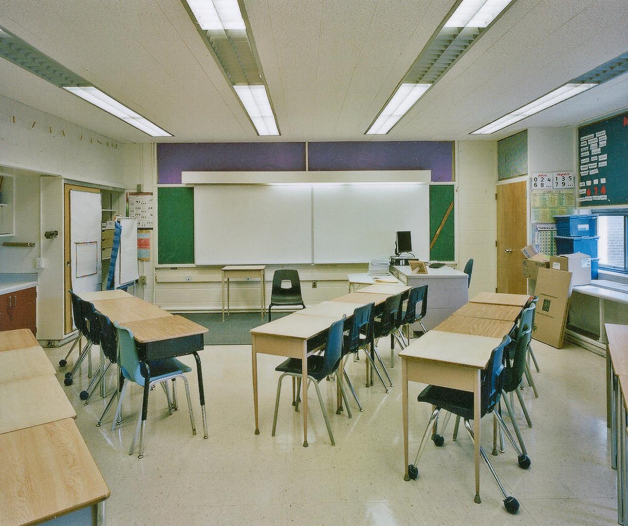 A photograph of a classroom, with desks, chairs and a whiteboard.