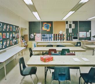 A view of a public school classroom, with tables, chairs and bulletin boards displaying artwork ...