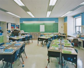 A photograph of a classroom, with chairs, tables, a chalkboard and shelving units.