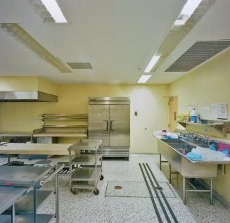 A photograph of a cafeteria kitchen, with a sink, refrigerator and metal tables.