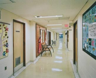 A photograph of a hallway in a public school, with benches and display boards.