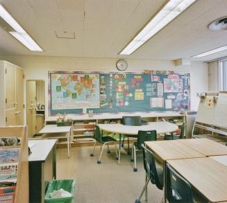 A photograph of a public school classroom, with desks, chairs, shelves and a chalkboard.