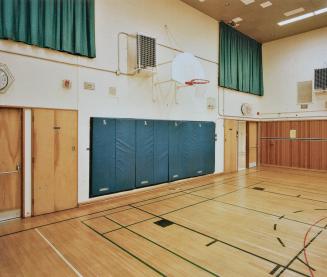 A photograph of a school gymnasium, with a basketball backboard and net.