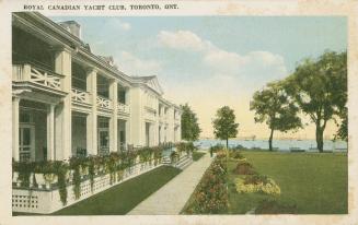 Colorize photograph of the front a a large building with a veranda. Manicures lawn; lake with b ...