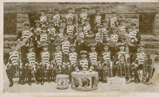 Black and white photograph of four rows of men in marching band uniforms posing with their inst ...